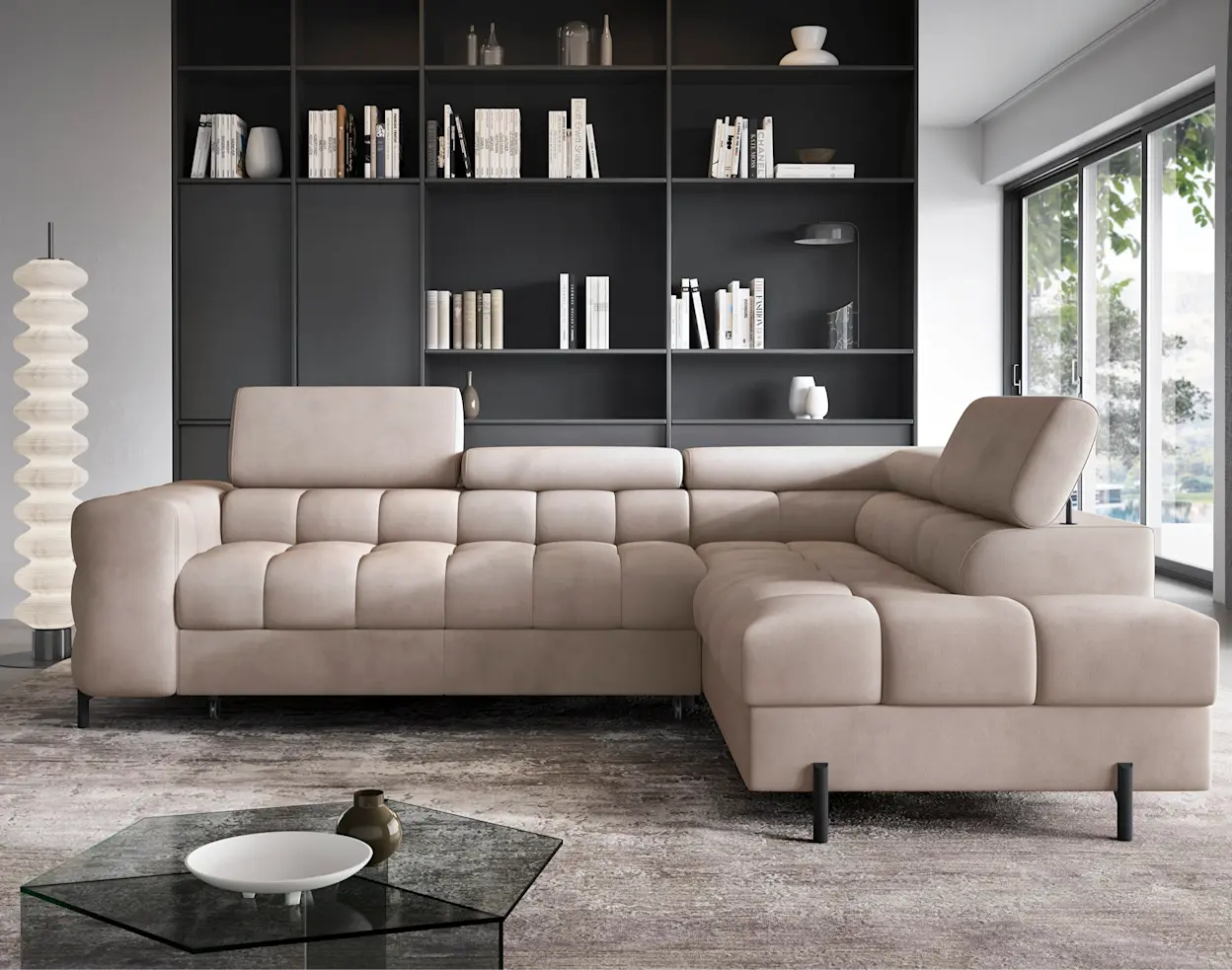 Beżowy narożnik Ferucce w tkaninie Paros 02 w nowoczesnym salonie z dużym regałem na książki w tle. Miękkie, pikowane siedzisko i zagłówki tworzą wygodne miejsce do odpoczynku, a wnętrze dopełnia duże okno.