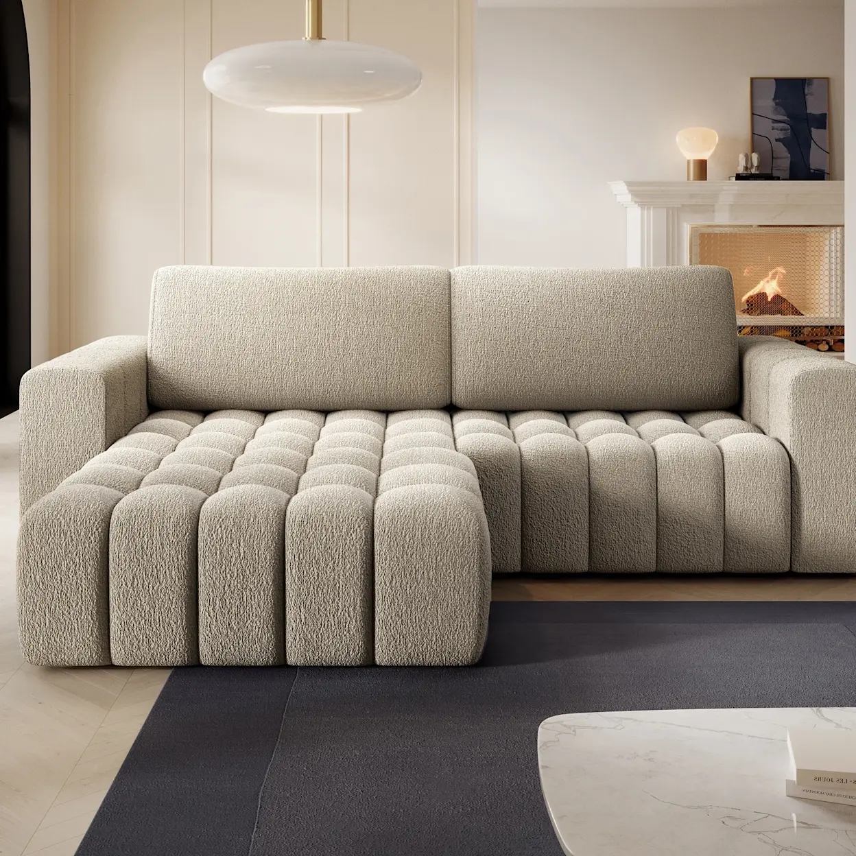 Narożnik Bonett Royal 20 w jasnym beżowym odcieniu, tapicerowany miękką tkaniną typu bouclé. Szezlong z przodu ma wyraźne, pionowe przeszycia, a całość tworzy przytulną strefę wypoczynku w salonie.