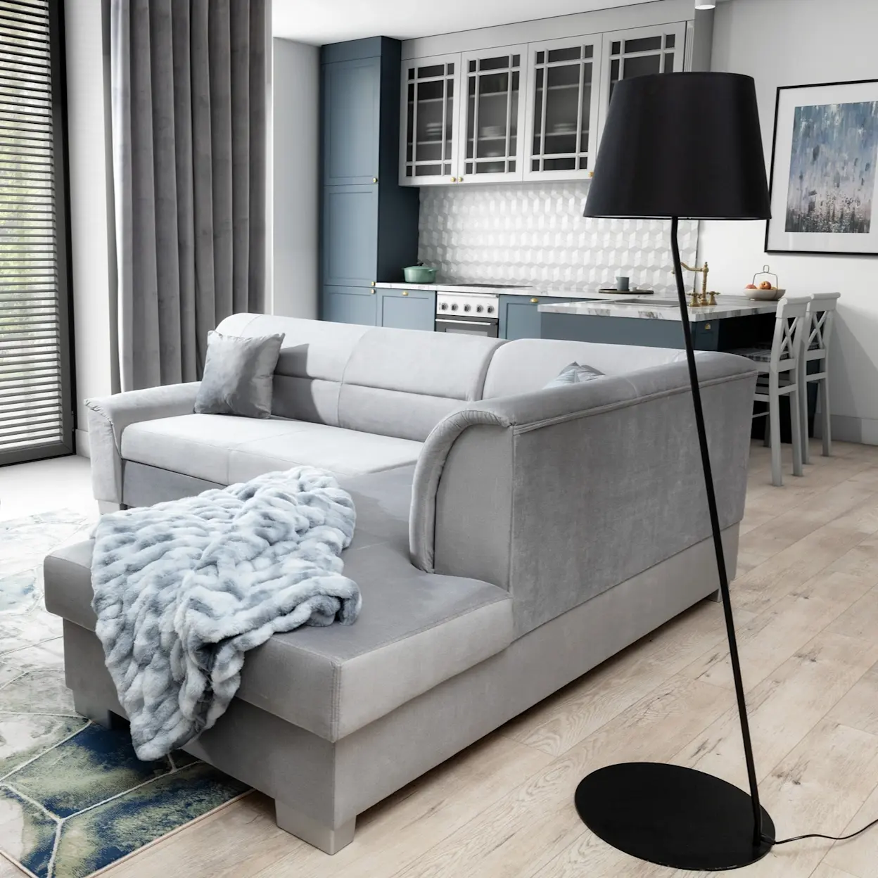 Szary narożnik Bergen Monolith 84 w salonie z aneksem kuchennym, z miękkim kocem na szezlongu i czarną lampą podłogową.
