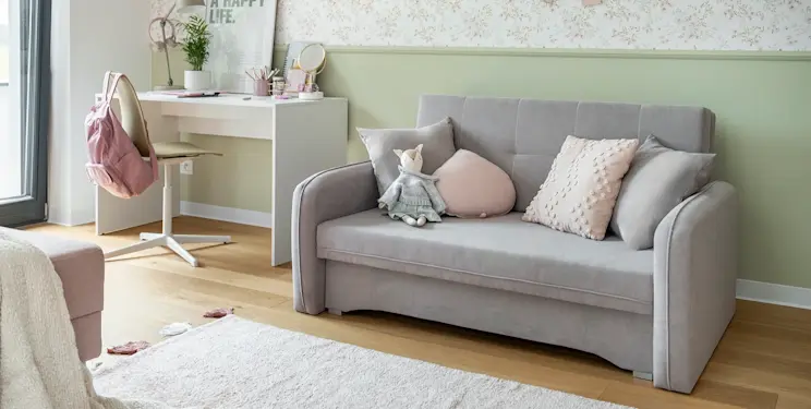 Jasny, przytulny pokój z kanapą Laine i biurkiem Nevy, udekorowany miękkimi poduszkami, pastelami i naturalnym światłem wpadającym z okna.