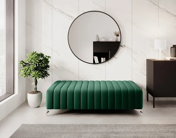 Aranżacja wnętrza z pufą Laurence w głębokiej zieleni, ustawioną na jasnej podłodze przy ścianie z delikatnym rysunkiem kamienia. W tle widać czarną komodę Lanzzi i dekoracje odbijające się w okrągłym lustrze Divissi, co dodaje przestrzeni lekkości.