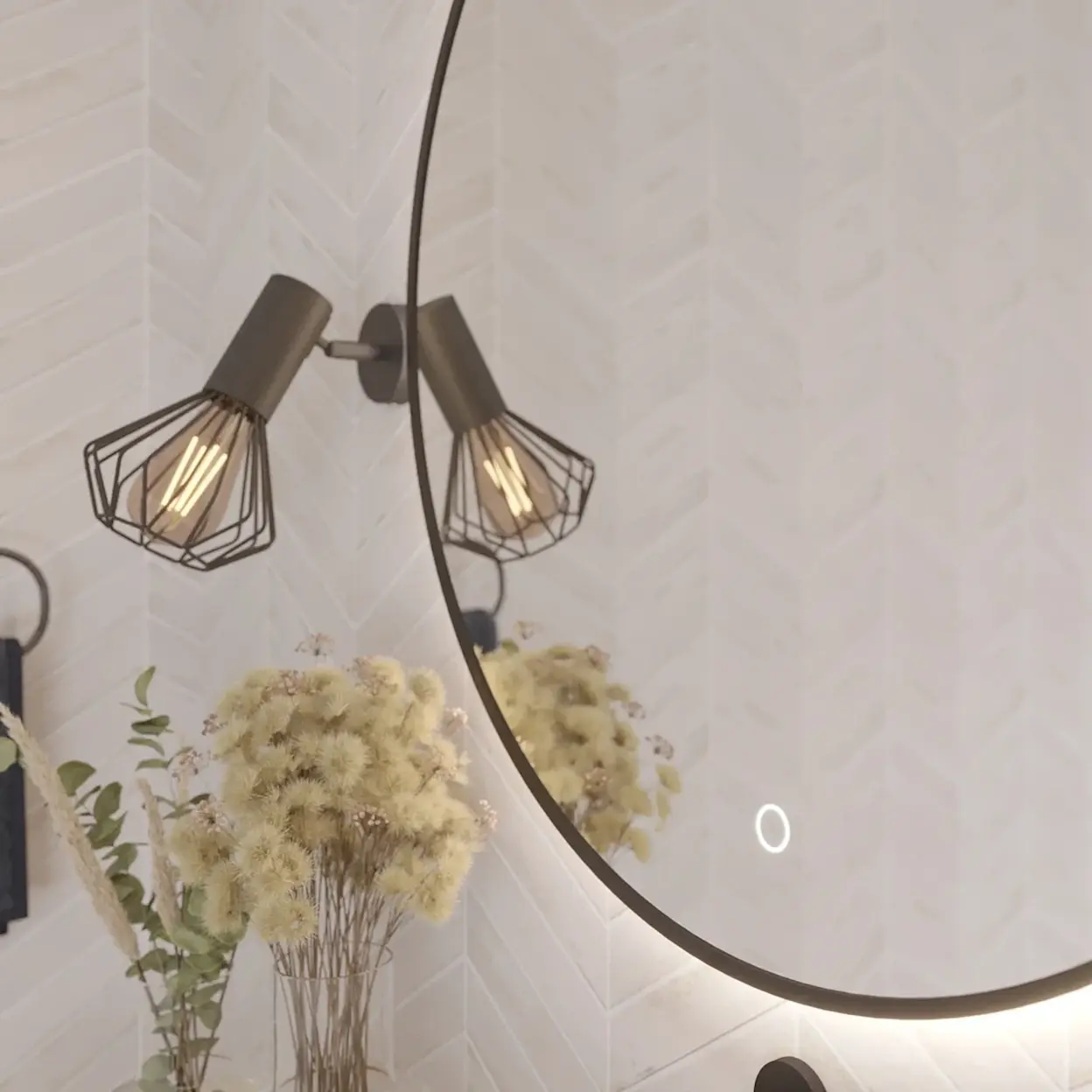 Zbliżenie na okrągłe lustro Orandiu z podświetleniem LED w łazience. W odbiciu widać kinkiety z industrialnymi kloszami i dekorację z suszonych kwiatów, a tło stanowią jasne płytki ułożone w jodełkę.