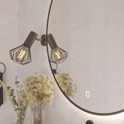 Zbliżenie na okrągłe lustro Orandiu z podświetleniem LED w łazience. W odbiciu widać kinkiety z industrialnymi kloszami i dekorację z suszonych kwiatów, a tło stanowią jasne płytki ułożone w jodełkę.