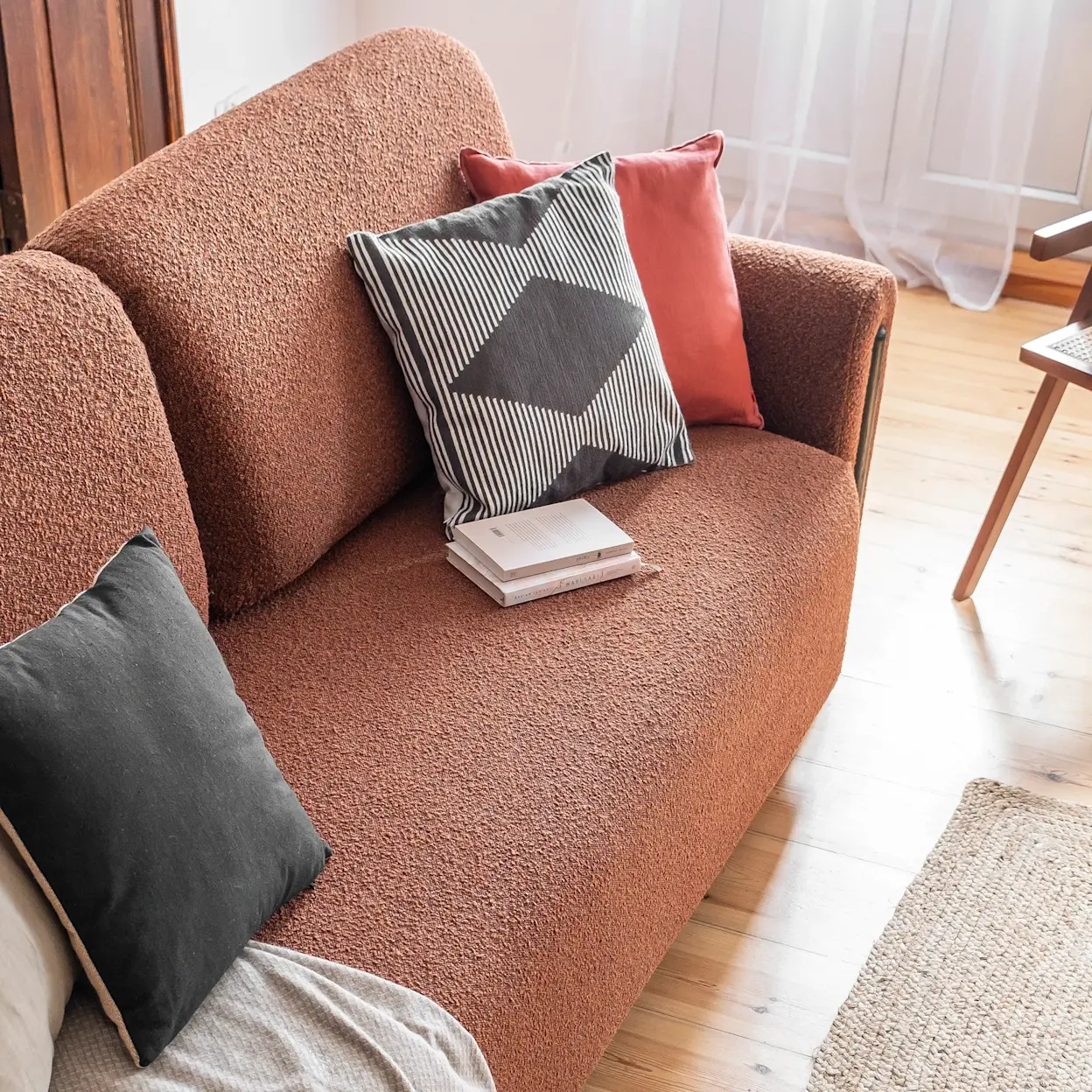 Zbliżenie na kanapę Arcadova w tkaninie Jaffray 30, ozdobioną poduszkami w różnych kolorach, w jasnym i przytulnym wnętrzu z drewnianą podłogą.