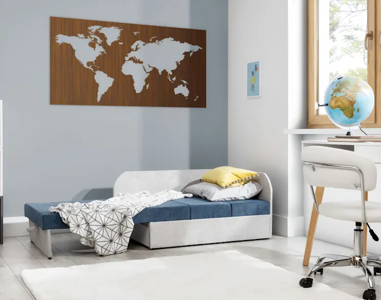 Kanapa Rosa w pokoju dziecięcym, rozłożona do spania – szaro-niebieskie siedzisko, poduszki i koc. W tle biurko przy oknie, globus oraz dekoracja mapa świata na ścianie, jasna i spokojna aranżacja.