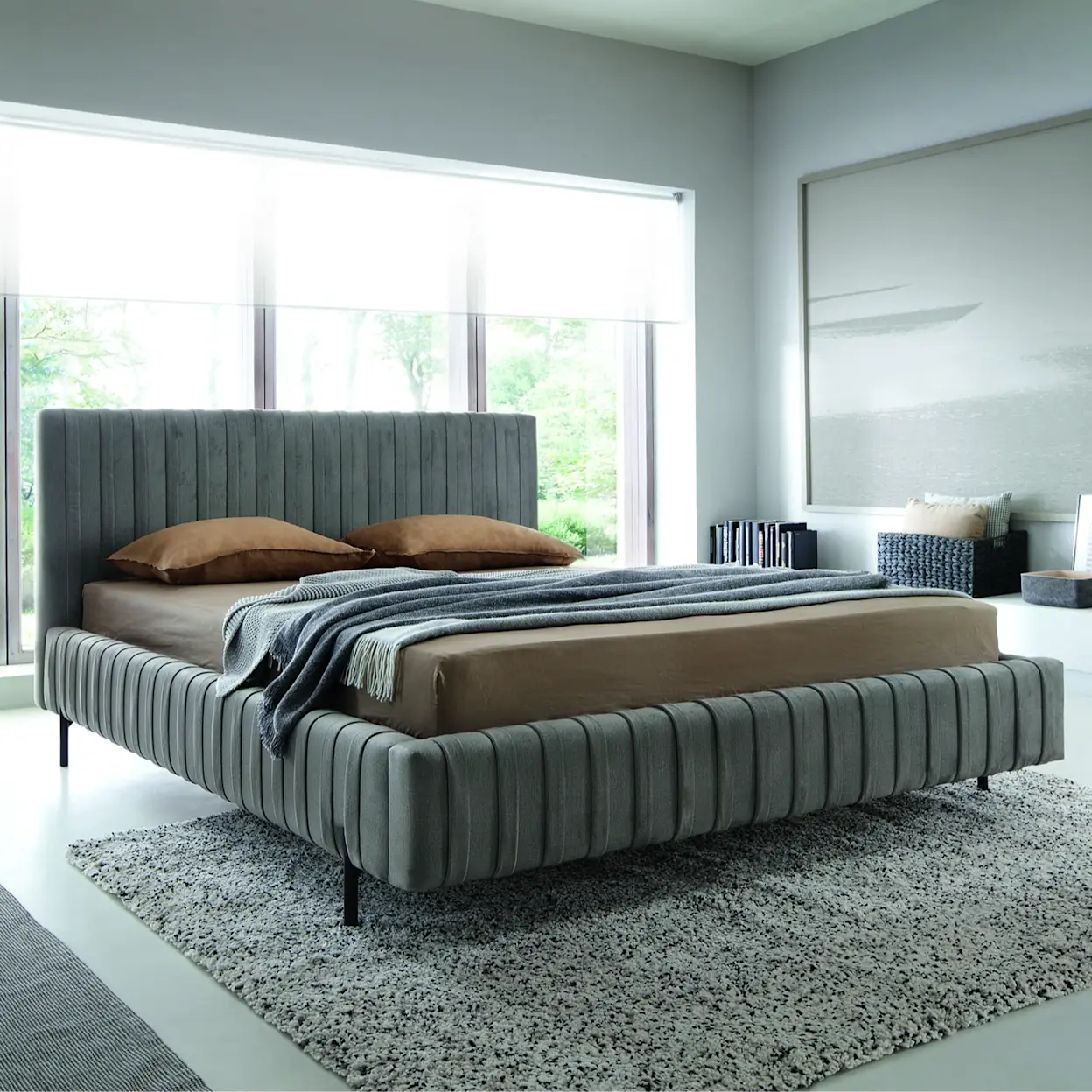 Tapicerowane łóżko Plissa z pionowymi przeszyciami, ustawione w nowoczesnej sypialni z dużym oknem i stonowaną kolorystyką.