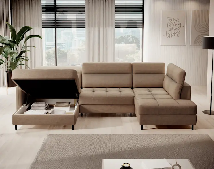 Beżowy narożnik Berrto w jasnym salonie z dużymi oknami i roletami. Sofa ma szezlong oraz otwarty pojemnik na pościel w lewym module, z widocznym miejscem na koce i tekstylia, idealnym do utrzymania porządku.