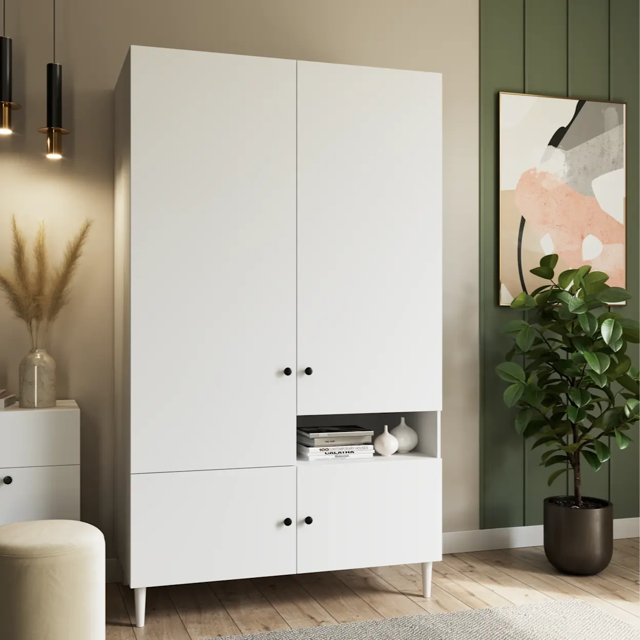 Szafa Dullum w kolorze białym ustawiona w jasnym salonie. Funkcjonalna bryła mebla, otwarta półka i eleganckie dodatki.