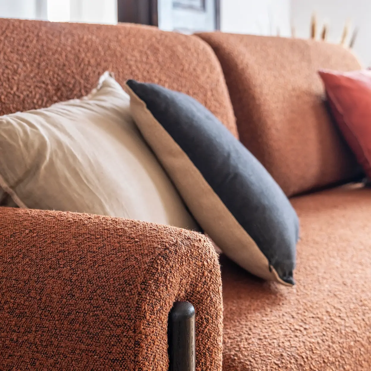 Zbliżenie na bok kanapy Arcadova w tkaninie Jaffray 30, z dekoracyjnymi poduszkami w naturalnych barwach, w przytulnym, jasnym wnętrzu.