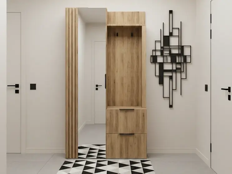 Garderoba Riganni do holu: drewniany moduł z wieszakami i pojemną szafką oraz pionowe lustro obok lameli. Wnętrze utrzymane w minimalistycznym stylu z białymi drzwiami, czarnymi klamkami i dywanem w trójkąty.