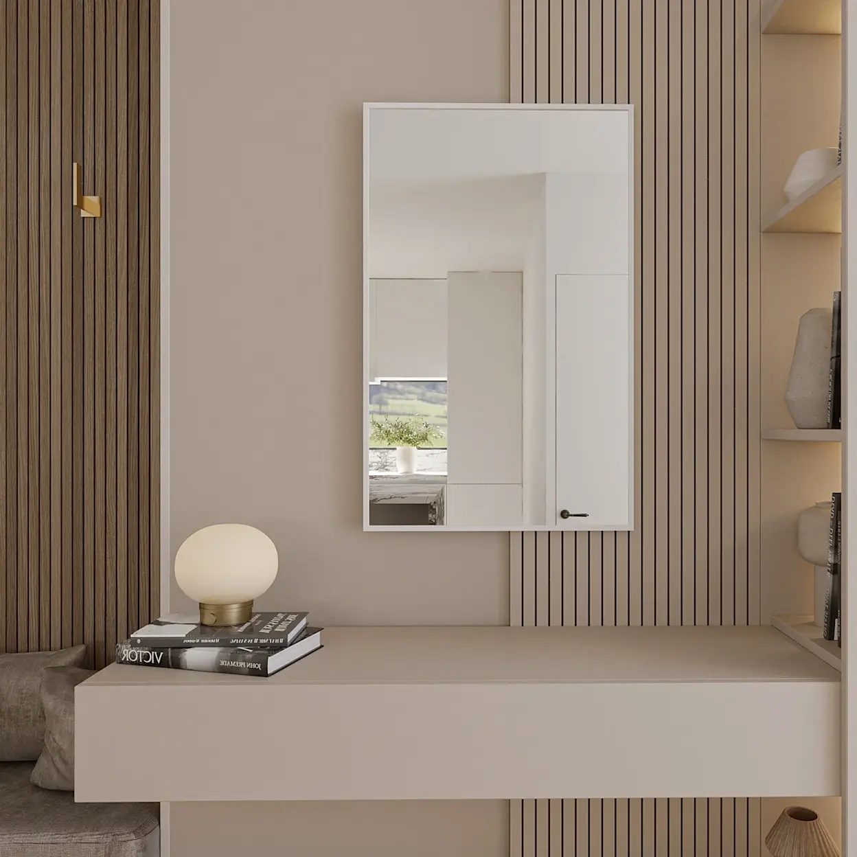 Lustro ścienne Fellan prostokątne w białej ramie zawieszone na tle pionowych lameli. Pod lustrem znajduje się minimalistyczna toaletka, a na blacie leży stos książek i stoi kulista lampka.