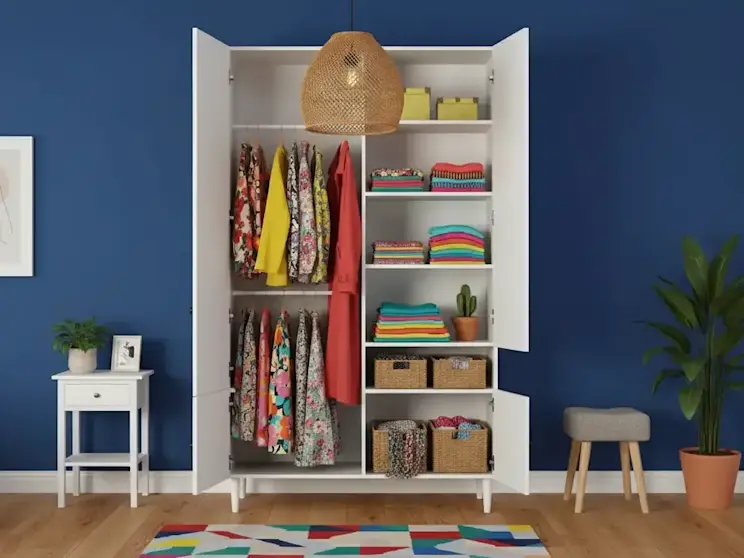 Nowoczesna biała szafa Dullum z funkcjonalnym wnętrzem, drążkiem na ubrania oraz półkami na złożone tekstylia i akcesoria, prezentowana w kolorowym pomieszczeniu z dekoracyjną lampą sufitową.