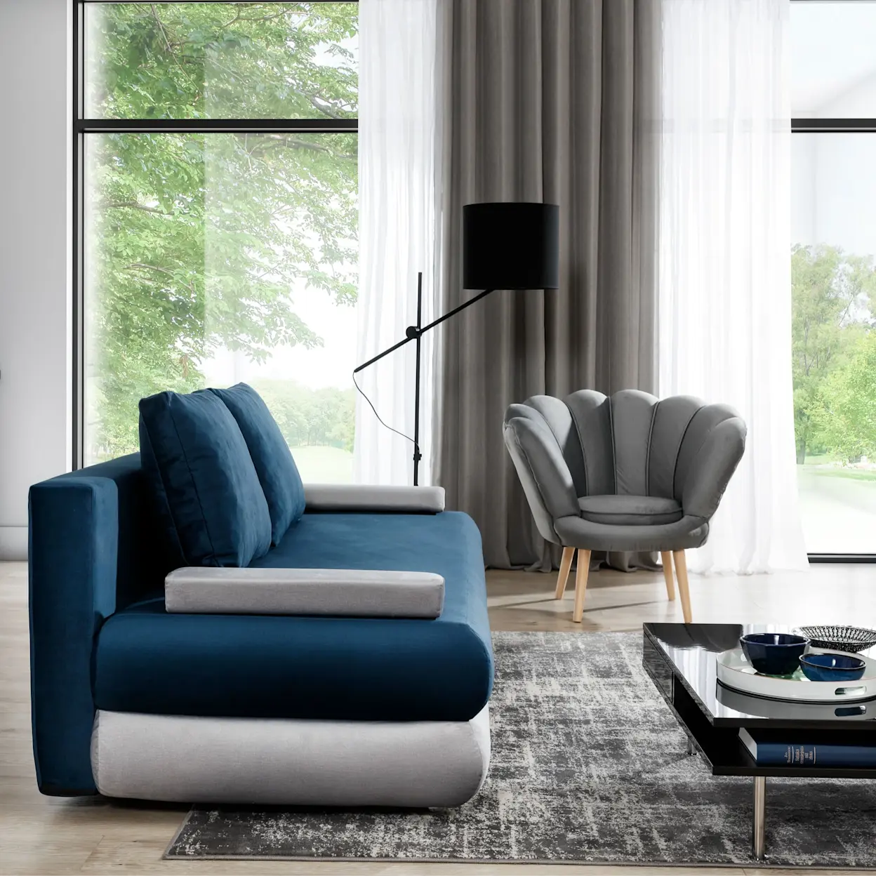 Granatowa sofa rozkładana Milo z szarymi podłokietnikami (Monolith 77/Monolith 84) w nowoczesnym wnętrzu. Obok stoi stolik kawowy z połyskiem, a za kanapą widać okno z widokiem na zieleń oraz miękkie, jasne firany.