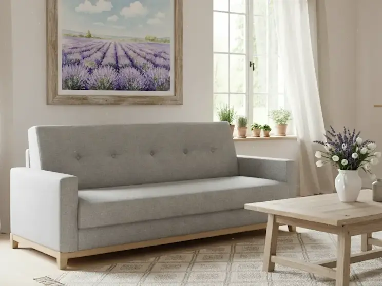 Szara wersalka Selene w tkaninie Sawana 21 z drewnianymi nóżkami w kolorze buk w jasnym salonie. Sofa stoi przy oknie z jasnymi zasłonami, a nad nią wisi obraz z lawendowym polem, tworząc spokojną i przytulną aranżację wnętrza.