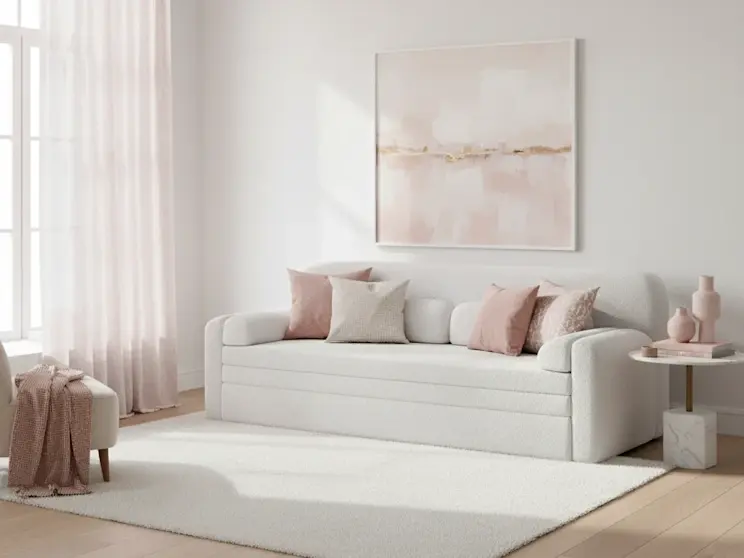 Biała sofa Elioss w tkaninie Royal 01, zaprezentowana w jasnym salonie z pudrowymi dodatkami i miękkim, naturalnym światłem.