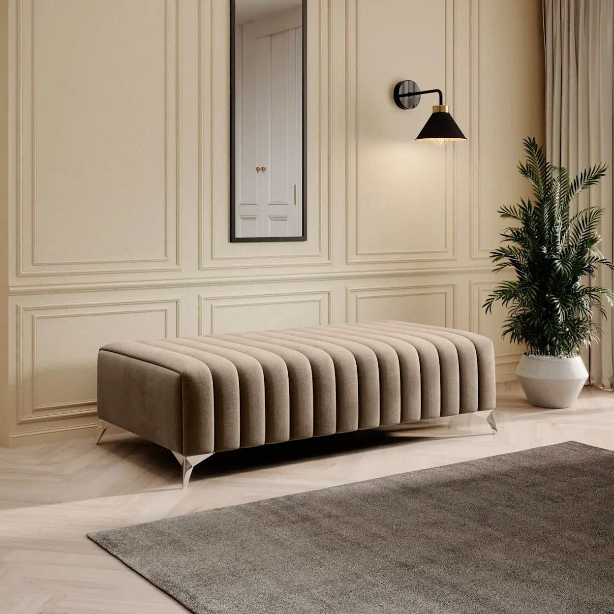 Beżowa pufa Laurence w tkaninie Monolith 76 ustawiona w eleganckim wnętrzu z jasną sztukaterią. Nad nią wisi lustro Arizona w czarnej ramie, obok świeci kinkiet Detmer, a na podłodze leży dywan Verlice Grey w stonowanym odcieniu.