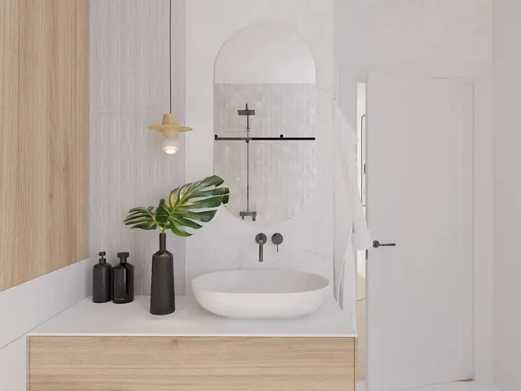 Lustro łazienkowe Nunisse bez ramy w kształcie owalu, zamontowane nad umywalką na jasnym blacie. Obok stoją ciemne dozowniki i wazon z liściem, a całość dopełniają białe płytki oraz czarne elementy armatury i prysznica.