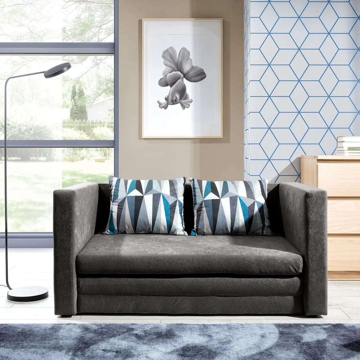 Kompaktowa kanapa rozkładana Neva w tkaninach Alova 10 i Lima 75, ustawiona w jasnym salonie jako wygodne miejsce do siedzenia i spania.