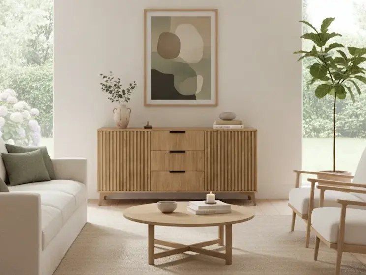 Neutralna komoda z lamelowanymi frontami Entsian ustawiona w jasnym salonie w stylu japandi. Naturalne drewno, minimalistyczne dodatki oraz duże okna z widokiem na ogród tworzą harmonijną i przytulną aranżację wnętrza.