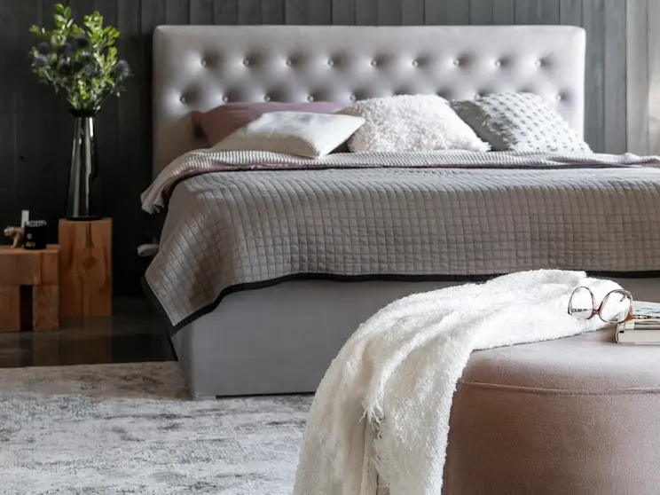 Stylowa sypialnia z łóżkiem kontynentalnym Loree z pojemnikiem. Szara tapicerka, dekoracyjne poduszki i naturalne dodatki podkreślają komfort.