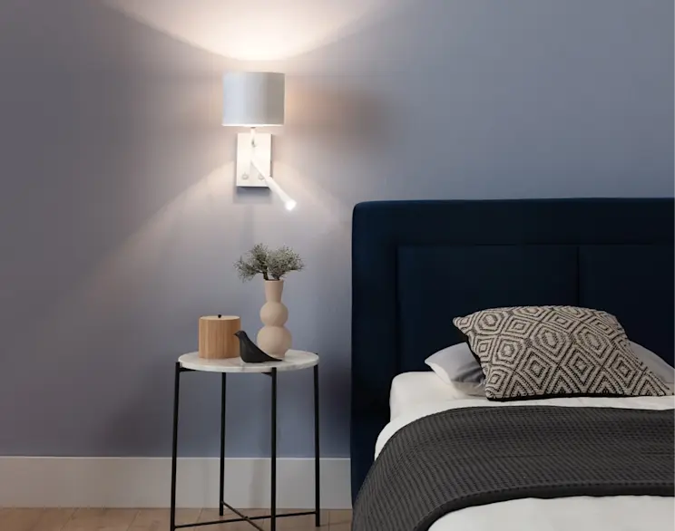 Biały kinkiet Vespillo z dwoma źródłami światła, zamontowany nad stolikiem nocnym w eleganckiej sypialni z granatowym zagłówkiem.