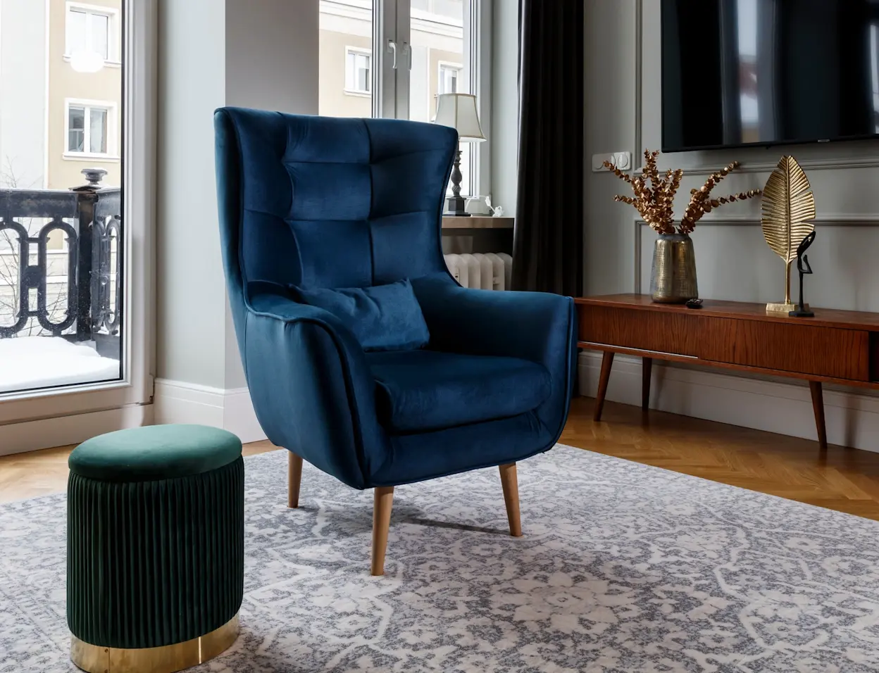granatowy fotel arti z poduszką i drewnianymi nogami ustawiony w eleganckim salonie z dekoracjami retro i dużym telewizorem na ścianie
