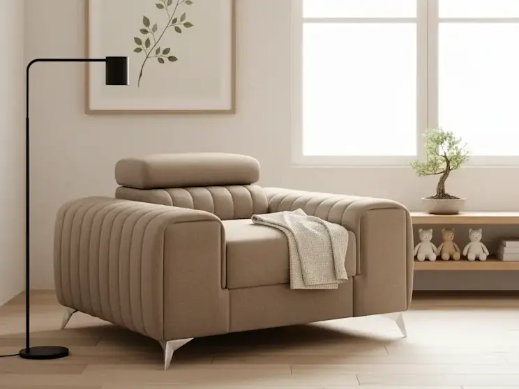 Beżowy fotel Laurence Nube 20 z pikowanymi bokami i zagłówkiem ustawiony w jasnym salonie przy oknie z minimalistyczną lampą podłogową.