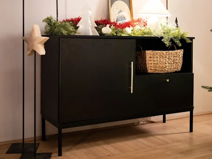 Czarna komoda Lanzzi ozdobiona świątecznymi dekoracjami, zielonymi gałązkami i lampką, tworząca przytulny, zimowy klimat we wnętrzu.