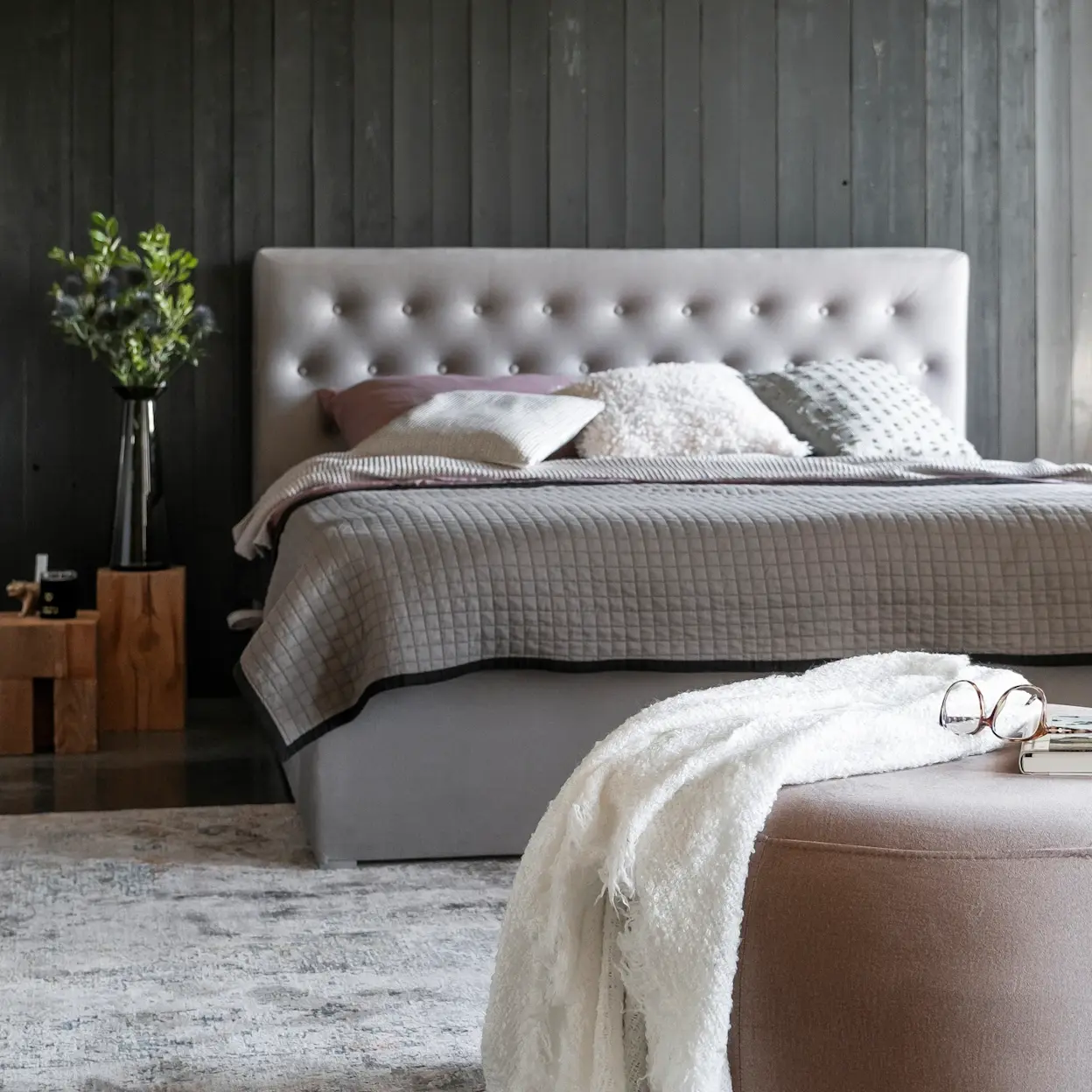 Pufa Bero Monolith 63 ustawiona w sypialni przy łóżku kontynentalnym. Miękka tapicerka i stonowana kolorystyka podkreślają elegancki charakter wnętrza.