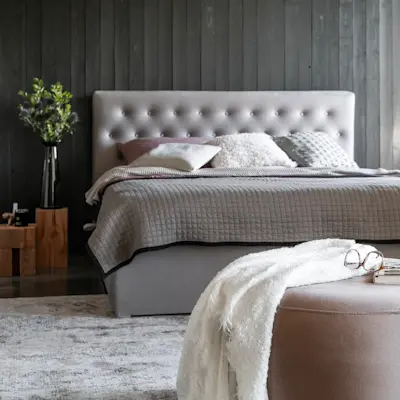 Pufa Bero Monolith 63 ustawiona w sypialni przy łóżku kontynentalnym. Miękka tapicerka i stonowana kolorystyka podkreślają elegancki charakter wnętrza.