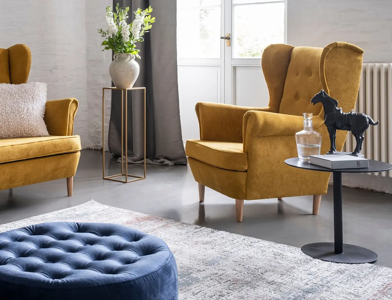 Salon ma prosty, ale przytulny klimat. Na środku znajduje się fotel w musztardowym kolorze oraz musztardowa sofa. Całość dopełnia pufa w kolorze granatowym