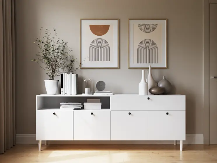Biała komoda Dullum w nowoczesnej aranżacji, ozdobiona książkami i ceramicznymi dodatkami, tworząca lekkie, harmonijne wnętrze.