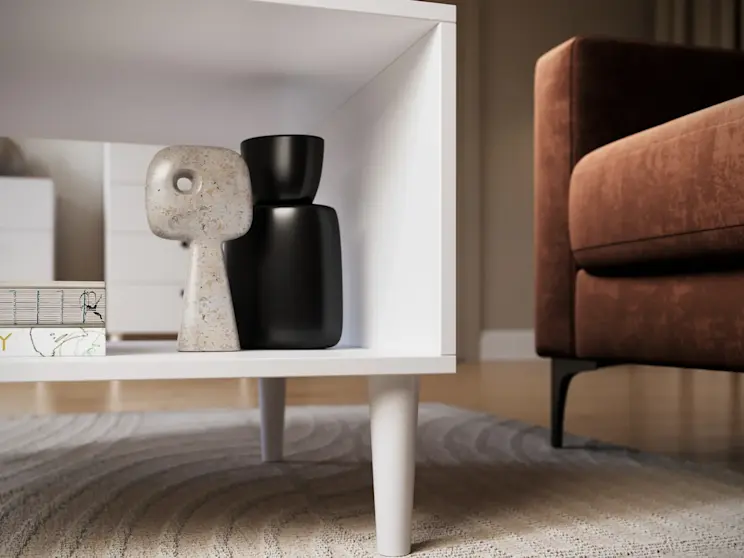 Biały stolik kawowy Dullum pokazany z bliska, z dekoracjami na półce i widoczną fakturą dywanu, tworzący elegancki i spokojny klimat wnętrza.