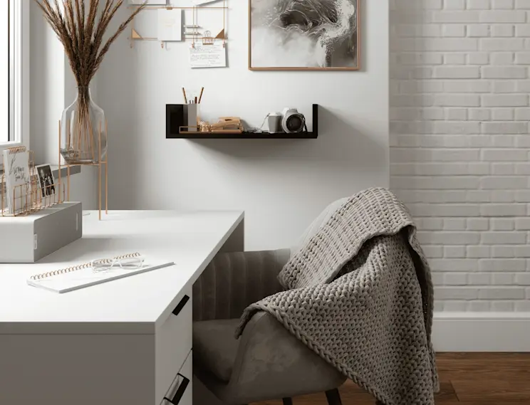 Biurko Barold i półka Vissta w jasnym kąciku pracy, z dekoracjami w złotych tonach, aparatem i wygodnym fotelem z pledem.