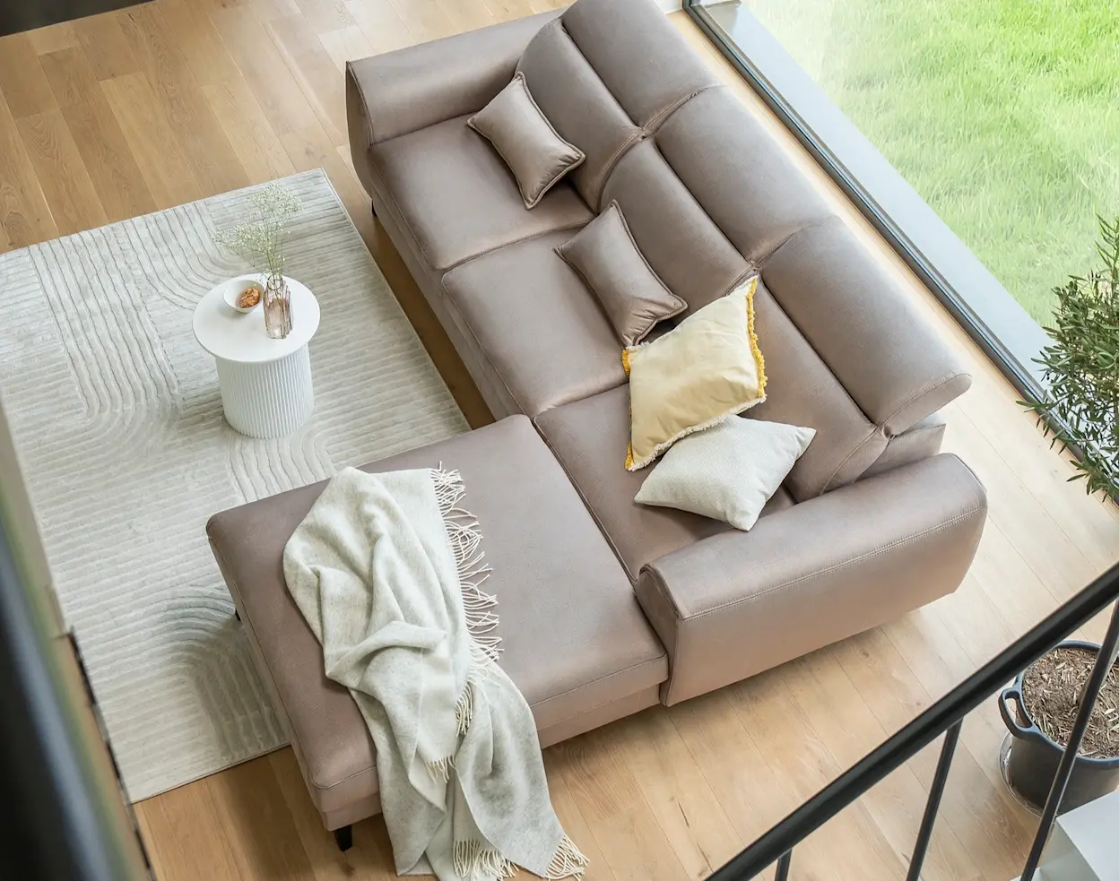 Beżowy narożnik Foble z poduszkami i pledem, ustawiony w jasnym salonie z dużym oknem i miękkim dywanem, tworząc przytulną strefę relaksu.