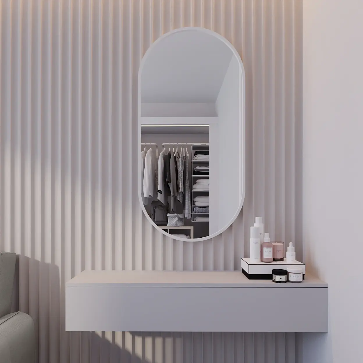 Białe, owalne lustro dekoracyjne Arducati na ścianie z jasnymi lamelami. W odbiciu widać garderobę z ubraniami na wieszakach i półkami. Pod lustrem znajduje się biała, wisząca półka/toaletka z kosmetykami.