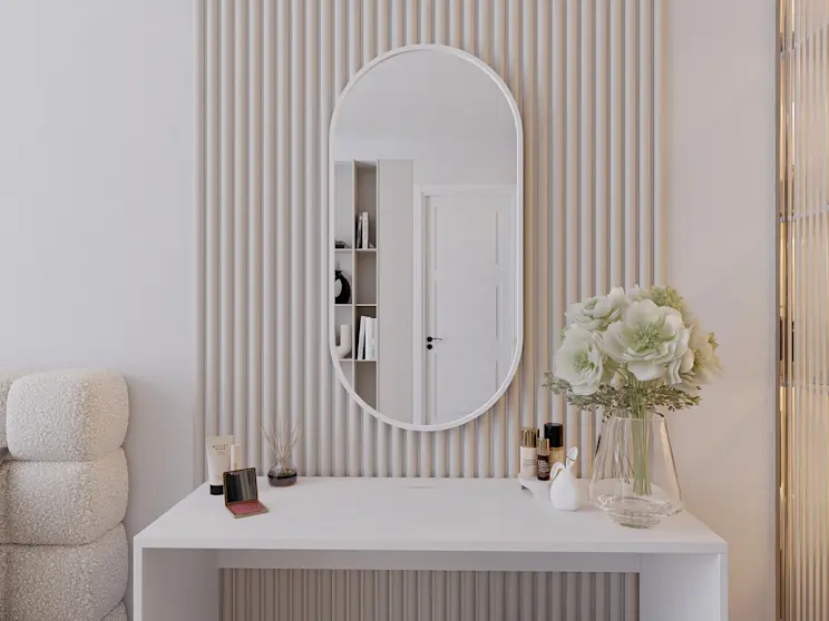 Jasna aranżacja kącika beauty: lustro dekoracyjne Arducati w białej ramie nad biurkiem Nevy. Na blacie widać perfumy, drobne akcesoria i duży wazon z bukietem, a w lustrze odbijają się drzwi i regał w tle.