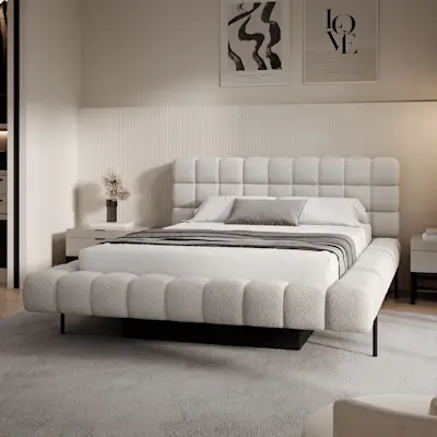 Tapicerowane łóżko Magentta w jasnym boucle z miękko pikowanym zagłówkiem i szeroką ramą stoi w nowoczesnej sypialni. W tle są jasne panele ścienne, dwie szafki nocne i plakaty nad łóżkiem.