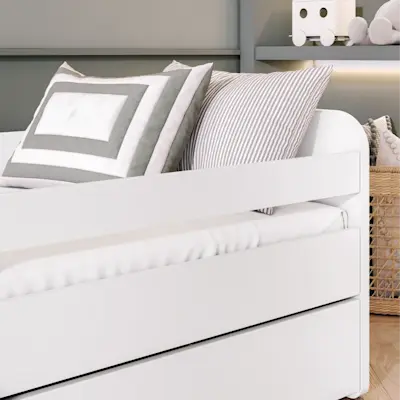 Zbliżenie na białe łóżko dziecięce Duuli z materacem, z widoczną barierką zabezpieczającą i miękkim posłaniem. Jasna kolorystyka oraz poduszki tworzą spokojną, przytulną przestrzeń do snu.