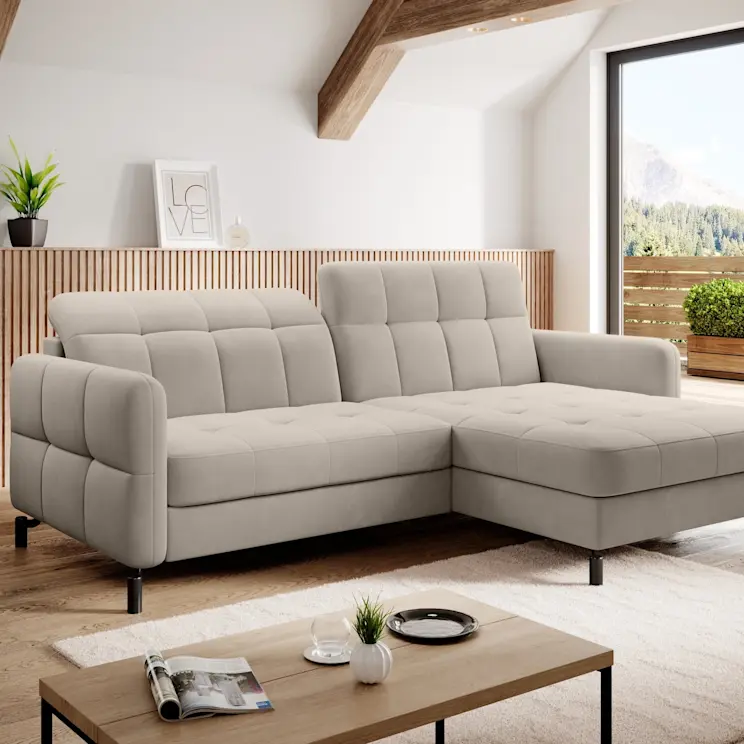 Jasny narożnik Lorelle Paros 02 w nowoczesnym salonie z dużym oknem i widokiem na góry. Sofa z szezlongiem ma pikowane siedzisko i oparcie, stoi na czarnych nóżkach przy stoliku kawowym.