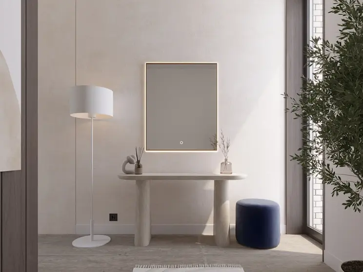 Lustro wiszące LED Vixisse z delikatną ramką świetlną w jasnym wnętrzu przy dużym oknie. Na blacie stoją dekoracje, obok ustawiono pufę Linsy oraz lampę stojącą Vespillo, tworząc funkcjonalną strefę do makijażu.