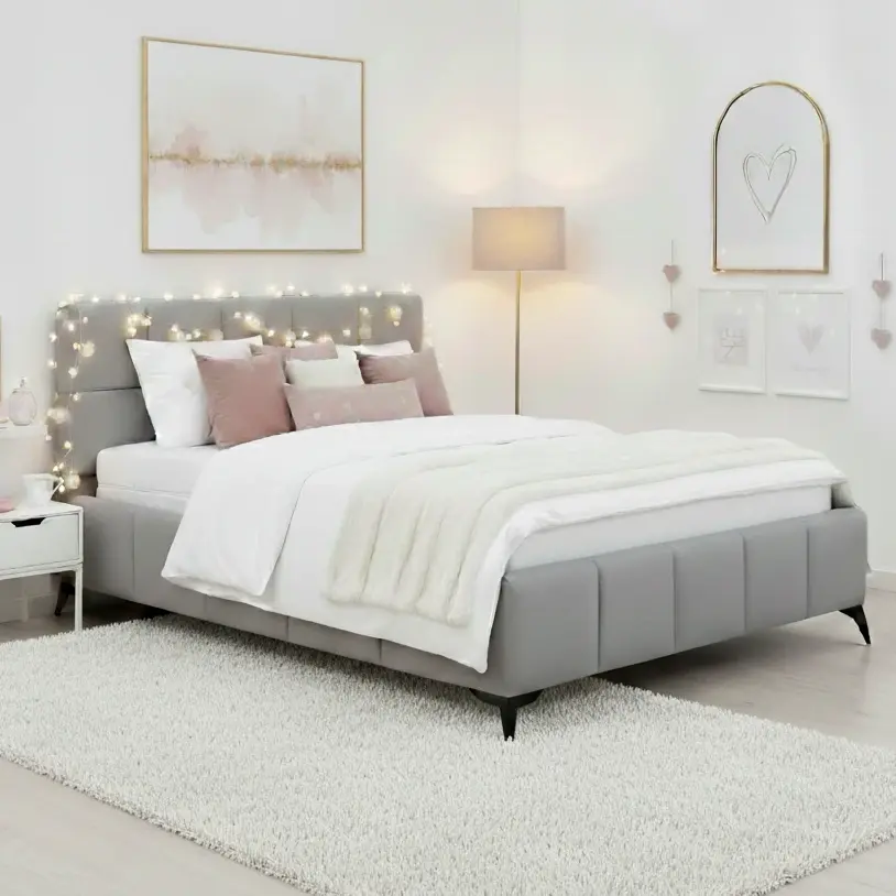 Jasnoszare łóżko tapicerowane Mist Nube 03 w rozmiarze 180x200 w jasnej sypialni. Wysokie wezgłowie ozdobione jest delikatnymi lampkami, a biała pościel i poduszki w pastelowych kolorach tworzą przytulny klimat.