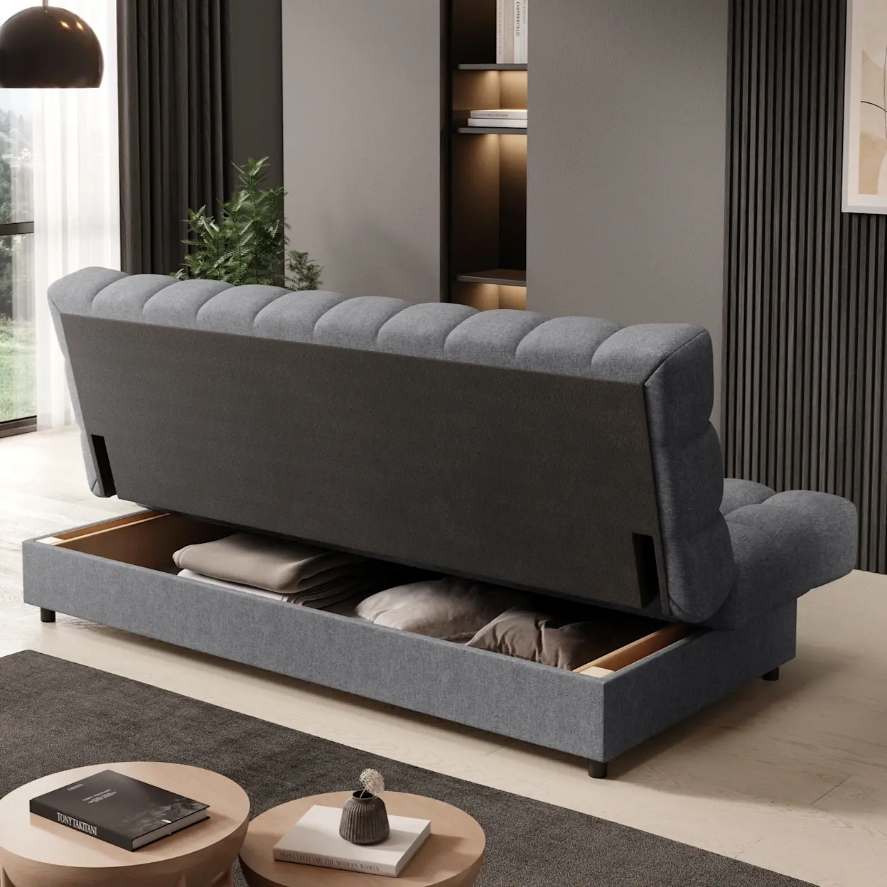 Szara wersalka Clareta Poco 04 z otwartym pojemnikiem na pościel, w którym ułożono koce i poduszki. Ujęcie od tyłu pokazuje pikowane oparcie oraz bryłę mebla w nowoczesnej aranżacji salonu.