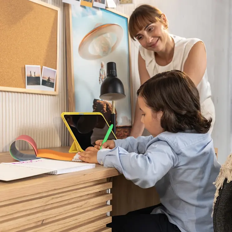 Chłopiec przy biurku Bisett pisze w zeszycie, a mama z uśmiechem towarzyszy mu w ciepłej aranżacji dziecięcego pokoju.