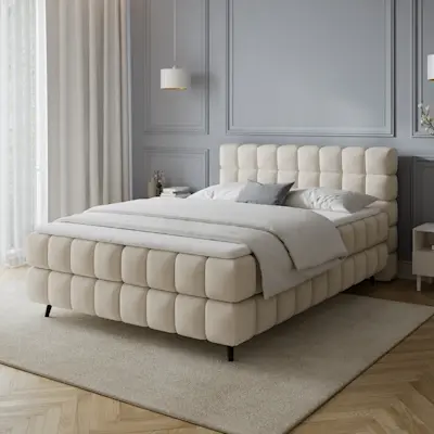 Łóżko kontynentalne Sabeno w tkaninie Calmora 18 w jasnej sypialni z szarą ścianą, dużymi oknami i minimalistycznymi dodatkami.