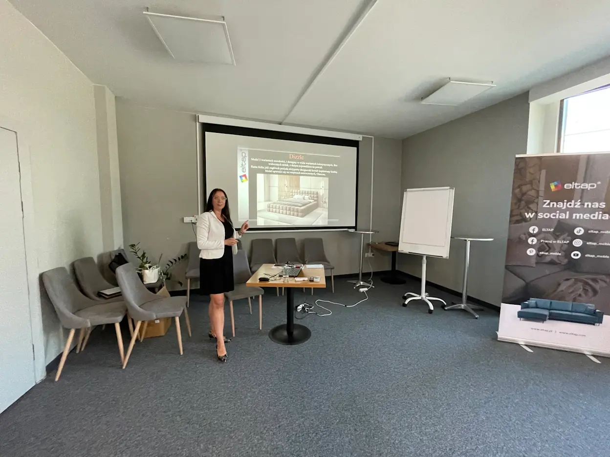 Architekt wnętrz prowadzi prezentację łóżka Dizzle podczas konferencji ELTAP, omawiając funkcjonalność i estetykę nowoczesnych rozwiązań.