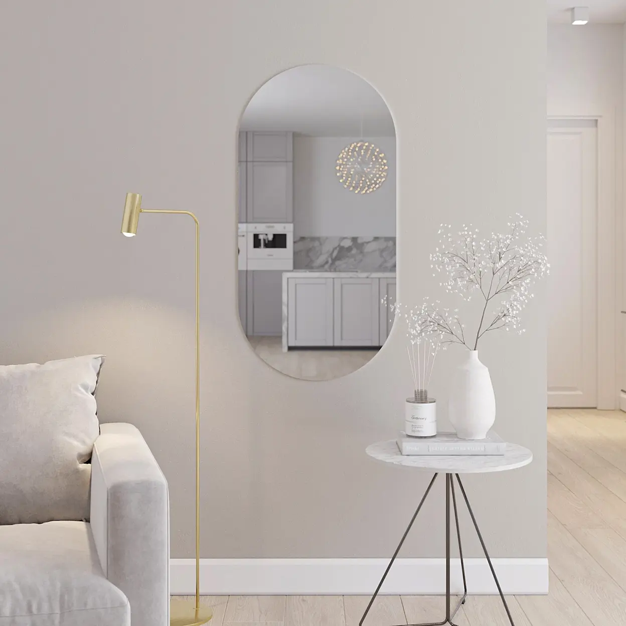 Owalne lustro ścienne Nunisse zawieszone na jasnej ścianie w eleganckim wnętrzu. W odbiciu widać kuchnię z jasnymi frontami i marmurowym wykończeniem, obok stoi stolik z dekoracjami i wazonem.