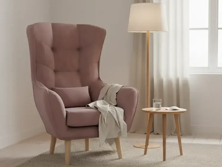Różowy fotel uszak Arti Matt Velvet 63 z pikowanym oparciem i drewnianymi nogami ustawiony w jasnym salonie obok stolika i lampy podłogowej.