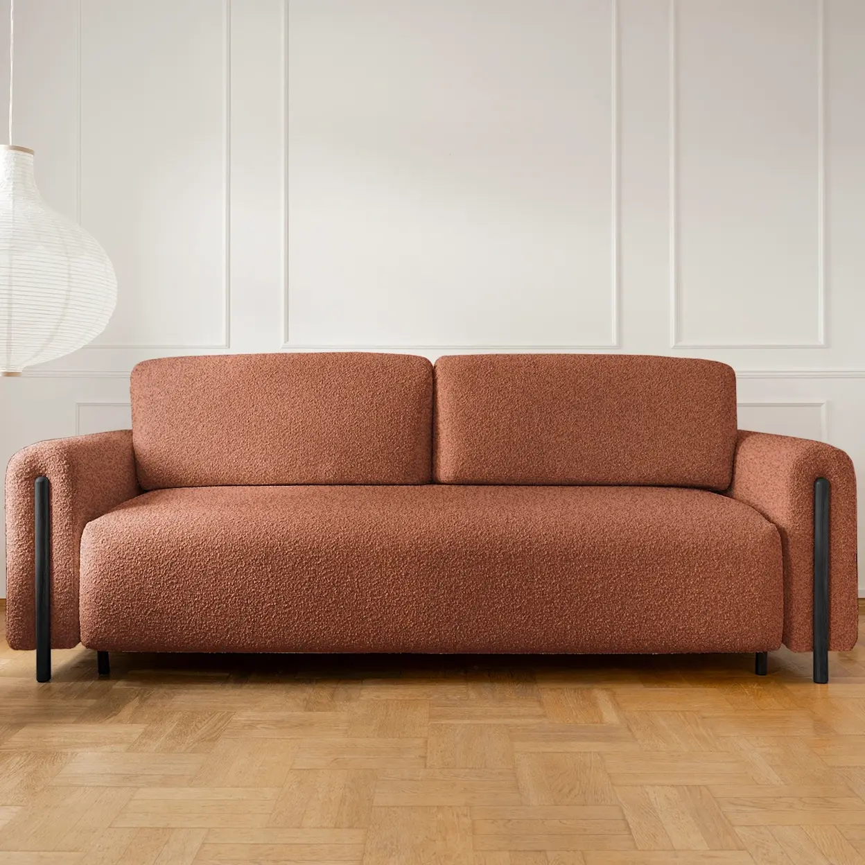 Nowoczesna kanapa Arcadova w rdzawym odcieniu, tapicerowana tkaniną boucle, ustawiona w jasnym salonie z eleganckimi panelami na ścianie.