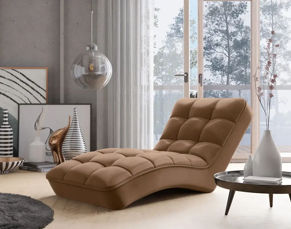 Szezlong Loren w kolorze roku 2025 w ciepłym odcieniu mocha mousse, z miękkim, pikowanym siedziskiem i profilowanym kształtem do relaksu. Leżanka stoi przy dużym oknie w jasnym salonie z dekoracjami i stolikiem.